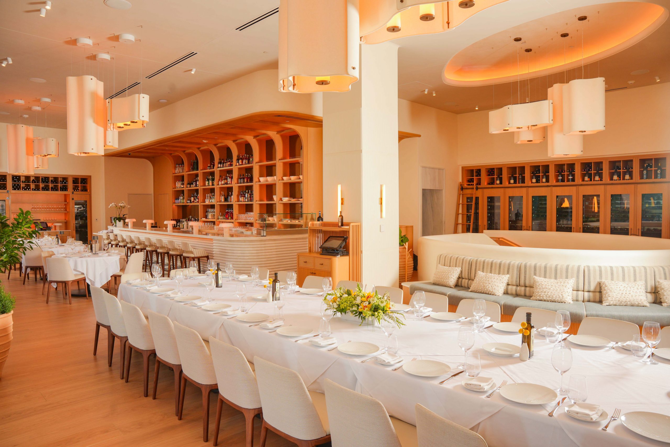 estiatorio milos private event space with long table setup, a full bar, additional small tables and banquette seating